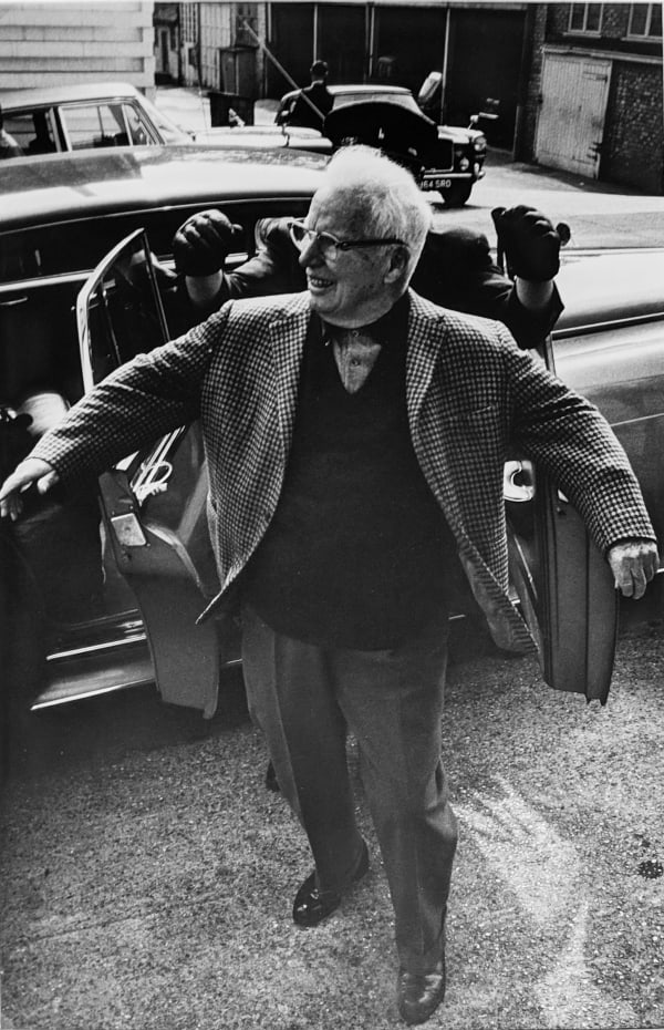 Black and white photograph of Charlie Chaplin walking outside from a car on the set of “A Countess from Hong Kong”