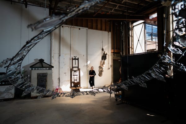 An artist, Marsha Pels, stands amongst sculptural works in a large industrial loft space