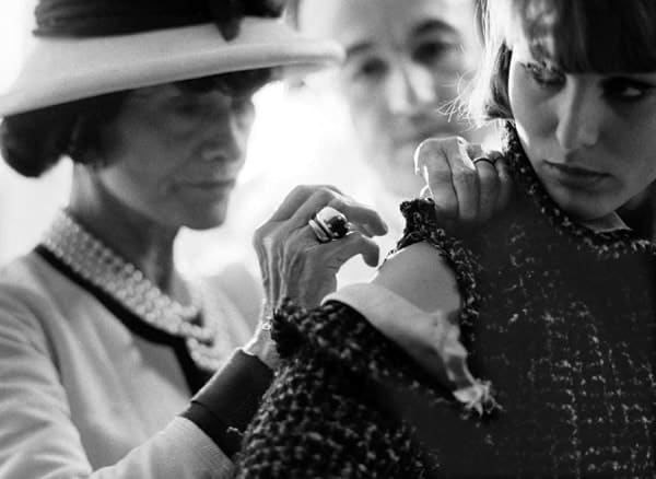 Black and white photograph of Mademoiselle Chanel creating designs for the upcoming August 1962 collections, draping and sewing fabric directly on the model