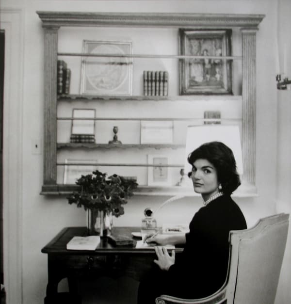 Black and white photograph of Jackie Kennedy sitting at her writing desk in her Georgetown house in Washington D.C.