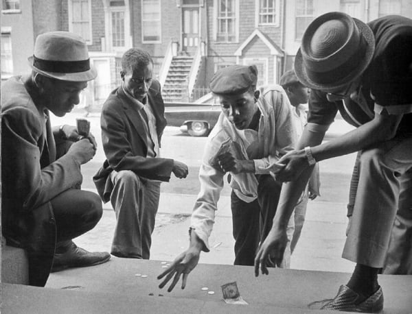 Black and white photograph of four men shooting craps outdoors on a stoop