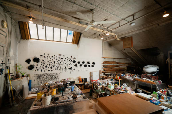 A loft studio space filled with work desks and art materials and with walls adorned with black sculptures by artist Gilda Pervin