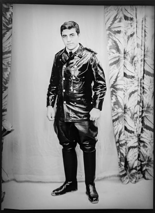1960s black and white photograph of a man in a leather suit standing in a photography studio