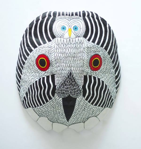 An intricately detailed owl with a striped geometric background is painted symmetrically on the back of a turtle shell entirely in black and white apart from two red and yellow circular markings on its wings, its blue eyes, and yellow beak.