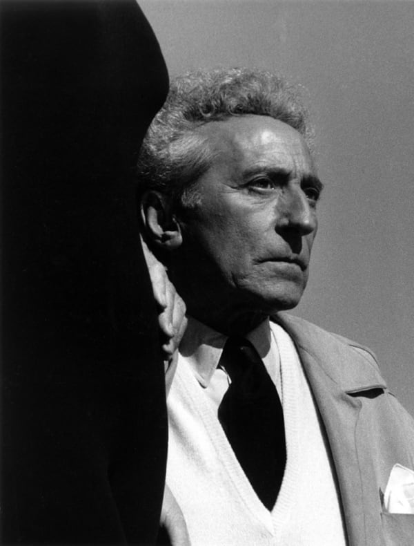 Black and white photograph of Jean Cocteau in a suit looking to the right with a dark shadow framing his left side