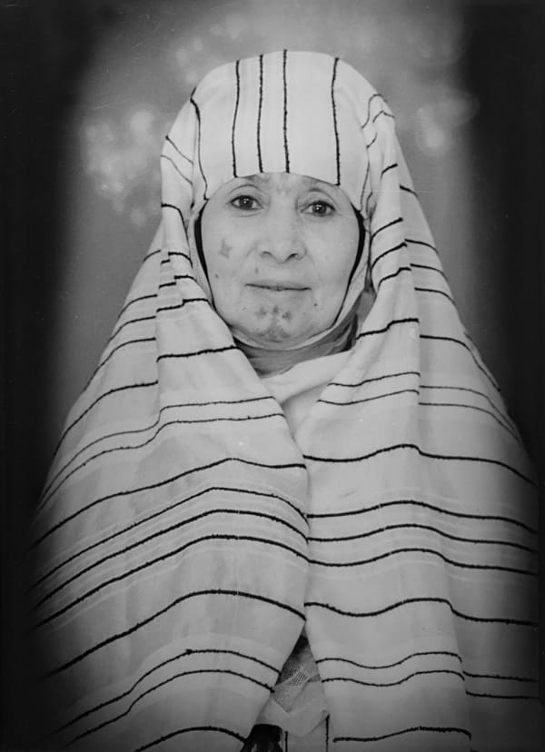 1960s black & white portrait of Amazigh woman with facial tattoos, wearing a striped head covering, in a photography studio