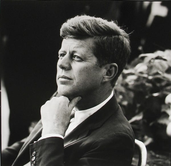 Black and white photograph of John F Kennedy at a three-quarters view as he rests his chin on his hand