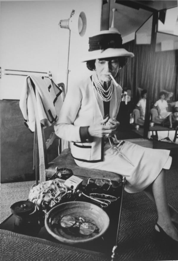 Black and white photograph of Designer Coco Chanel sitting and smoking a cigarette in the House of Chanel Paris