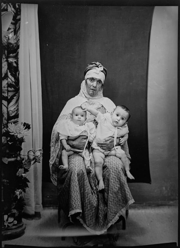 1960s black and white photograph of a woman sitting down and holding two babies in her arms