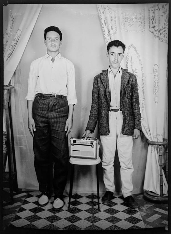 1960s black and white photograph of two men standing with a radio on a stepstool in between them