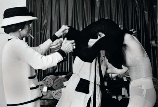 Black and white photograph of Designer Coco Chanel helping a model undress