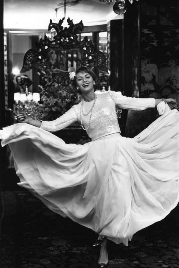 Black and white photograph of a model wearing a white Chanel dress and twirling so the dress spans out, smiling and laughing