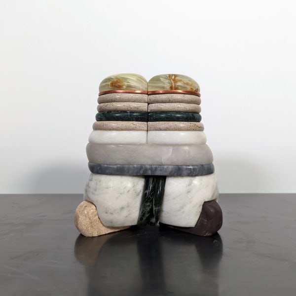 Split multilayer sculpture with black and brown base pieces, neutral layers, and a green and brass top