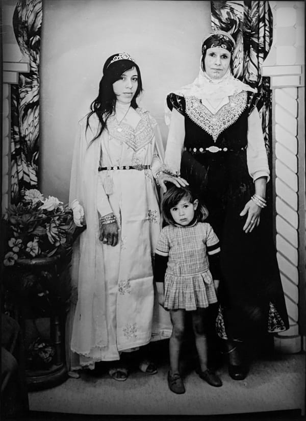 1960s black and white photograph of two women and one young girl, woman on the left is wearing a white embroidered dress and the woman on the right wears a black embroidered dress