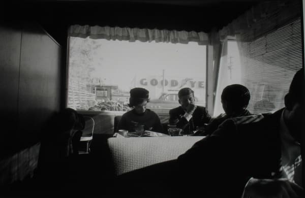 Black and white photograph of Senator John F Kennedy, Stephen Smith, and Jacqueline Kennedy having breakfast in a diner booth with their backs to a window while on the campaign trail in Oregon