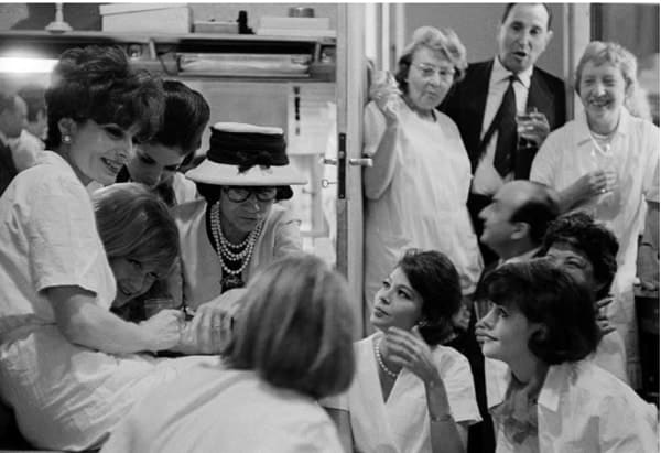 Black and white photograph of Designer Coco Chanel and models and staff during a celebration after the défilé in the House of Chanel