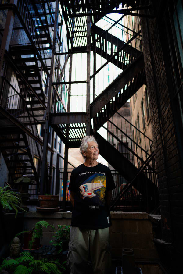 An artist, Gerald Marks, standing beside potted plants in front of fire escape steps outside his loft art studio in Midtown
