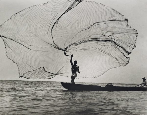 Black and white photograph of the silhouette of a fisherman casting a net off of a boat in Magdalena, Colombia