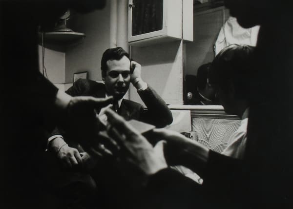 Black and white photograph of Ed Sullvan speaking to the Beatles at his desk, with two of The Beatles’ hands in the foreground and Ed looking at them in the background