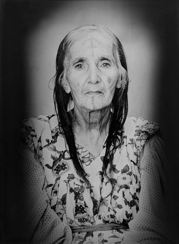 1960s black & white portrait of Amazigh woman with facial tattoos, wearing a floral dress, in a photography studio