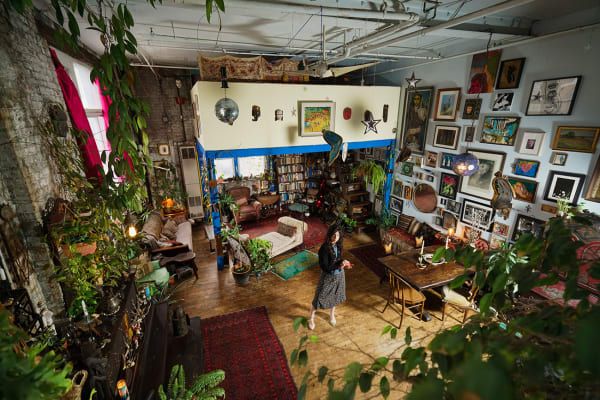 An artist, Jennifer Charles, standing in the center of her loft studio adorned richly adorned with pictures and plants