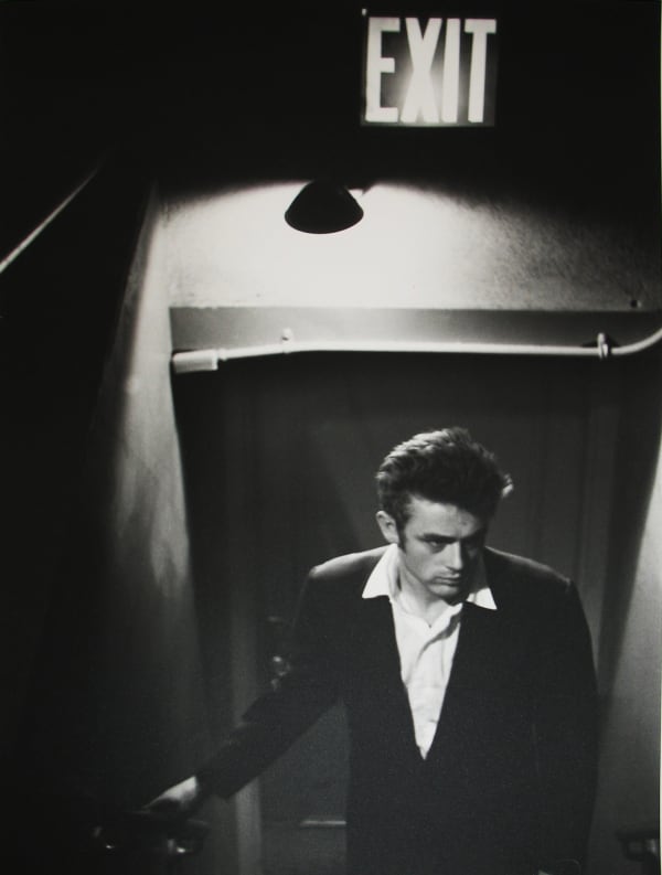 Black and white photograph of James Dean in a doorway underneath a lamp and Exit sign at ABC Studios