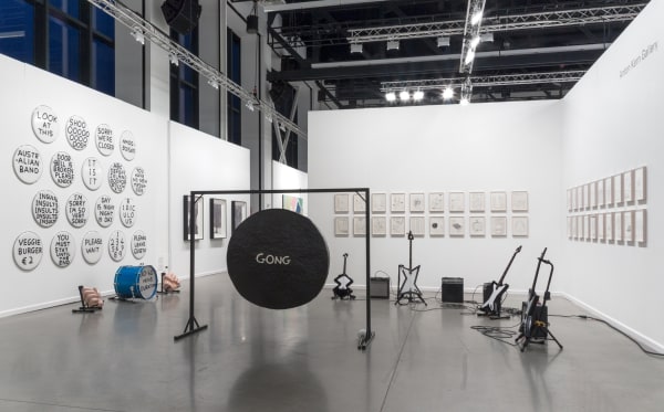 David Shrigley solo booth at the Independent Art Fair, with drums, a gong, and drawings.