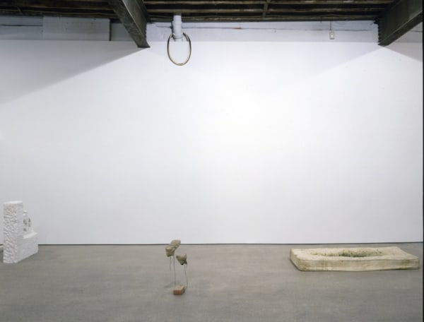 Installation view of Richard Hughes' first solo show in the U.S. Stones, paint buckets, worn out shoes, a dirty mattress, and rotten barrel planters occupy the gallery installation. Mattress and other objects featured.