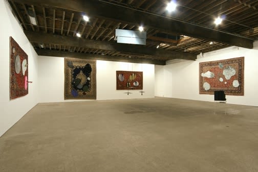 Installation view of Jim Lambie's fourth solo show at Anton Kern Gallery, consisting of five modified wall tapestries and an assemblage-like floor sculpture and video.