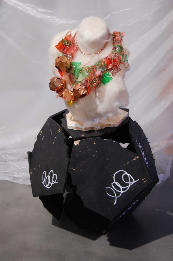 Black sculpture with white bust on top of it wearing a floral wreath
