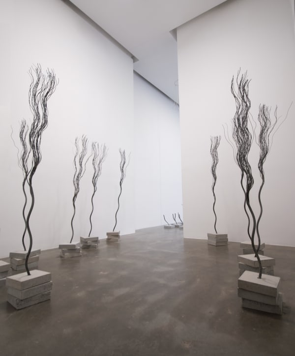 An installation view of several tree like sculptures made of wire rope planted in stacked concrete slabs