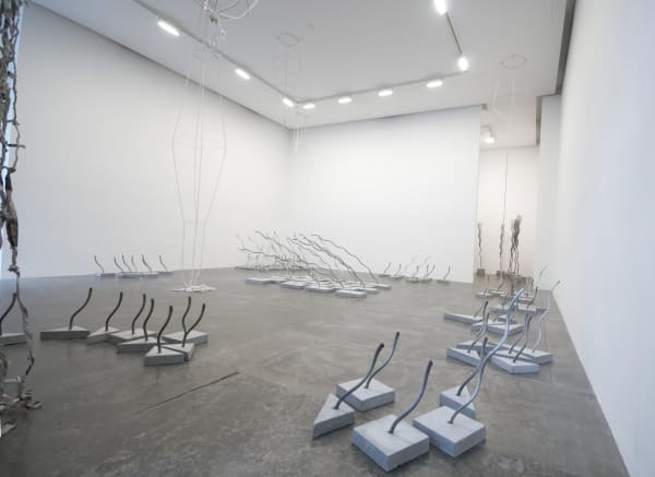An installation view showing several arrangements of sculptures made of wire rope embedded into concrete bases as well as a curtain of twisted newspaper and a rope and wire sculpture hanging from the ceiling 