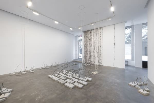 An installation view of Process showing many wire ropes embedded into concrete bases and a curtain of twisted newspaper on the wall