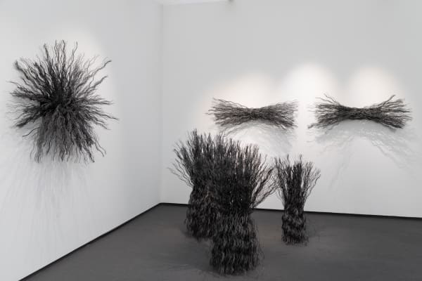 Installation view Maren Hassinger's Frieze Masters presentation of three bush-like sculptures made of wire rope grouped together on the floor with two sheaf-like wire rope sculptures and one starburst-shaped wire rope sculpture hanging on the wall