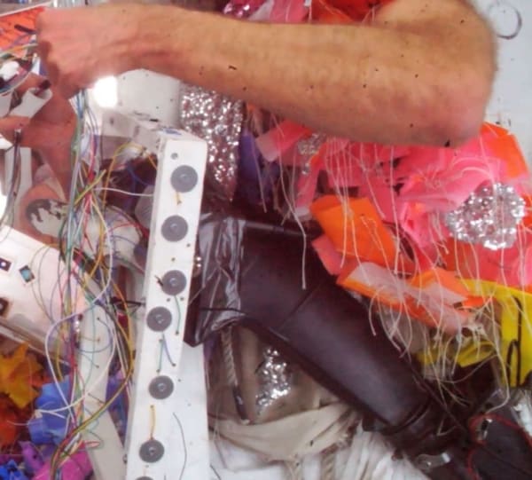 Structure created from studio detritus, with the artist's arm wrapping around it