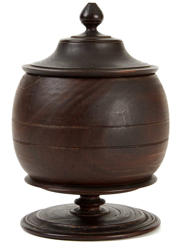 Sugar Bowl, late 18th century Turned lignum vitae with original finish 7 x 5 in. (17.8 x 12.7 cm) [height x diameter] (ArU 489) $ 5,000 ••• Turned with elegant precision, each curve in this sugar bowl flows seamlessly into the next to form a symphony in lignum vitae—a dense, almost indestructible wood prized for its rich color and natural oils that deepen over time. The design is leagues ahead of its time: a near-perfect sphere balanced on a turned base that subtly elevates it, giving it an inconspicuous sense of dignity that reflects the attention and care surrounding sugar’s role in daily life. The original finish has the soft sheen of age, imbuing the wood with a richness that speaks to the material's natural beauty. The lid, with its snug fit and small, tear-shaped finial, is as meticulously crafted as the body, creating a harmonious whole. This object possesses a quiet monumentality, yet it feels almost weightless, as if it could float off the surface beneath. It encapsulates both purpose and presence—a work of art hiding in plain sight.