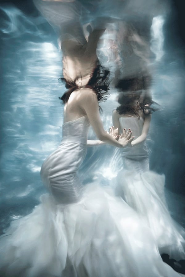 Barbara Cole photo of faceless woman underwater in a wedding dress touching her reflection.
