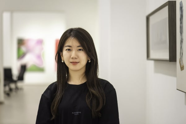 portrait of artist Zhang Xiaoli standing next to her artworks