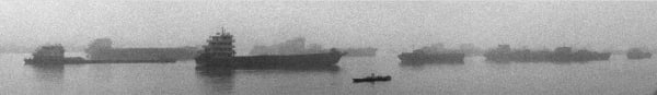 A few cargo ships are parked on the river surrounded by fog