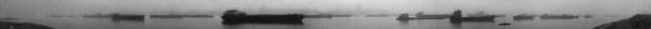 A few cargo ships are parked on the river surrounded by fog
