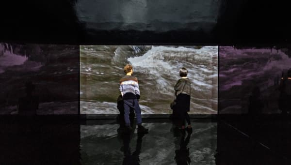 There are two viewers standing in front of the interior projection of landscape