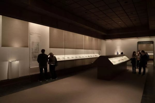 The museum's exhibition hall, with a long display case in the middle and transparent display tables on either side that also hold scrolls