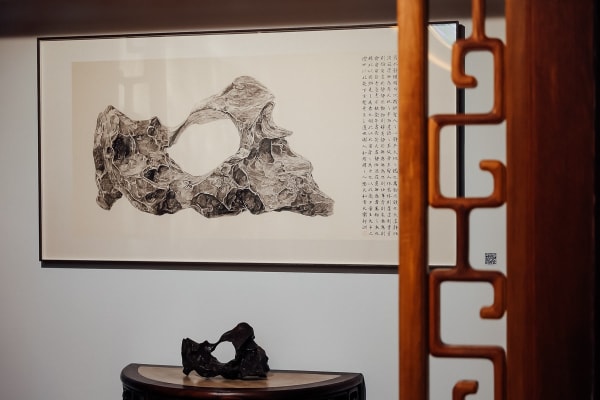 A painting of a literati stone hangs on the wall, and a table in front of it holds the literati stone in the picture