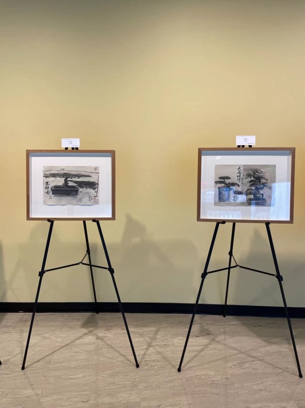 two charcoal artworks depicting pine needle trees by Tang Ke, exhibiting on tripod stands