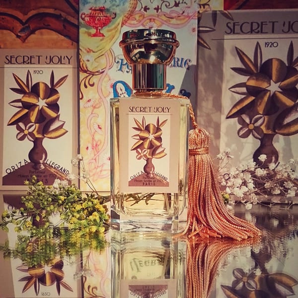 A perfume bottle SECRET JOLY by Oriza L. Legrand standing on a mirror with packaging on the background