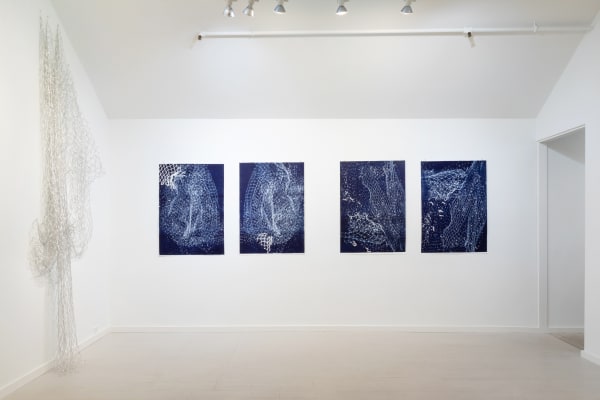 One silver net and four blue and white monoprints by Alice Hope installed closely together on white gallery walls.