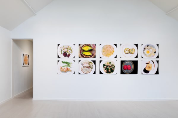 A group of horizontal Jack Ceglic works on one wall facing the viewer in an organized salon hang, with a door open leading towards another work.