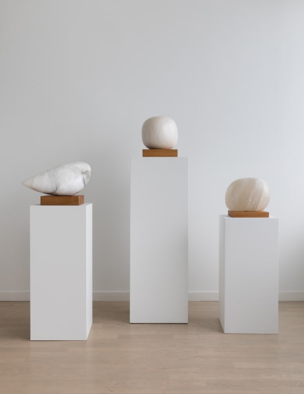Three alabaster Aya Miyatake sculptures on plinths at varied heights, the center plinth the tallest of the group.
