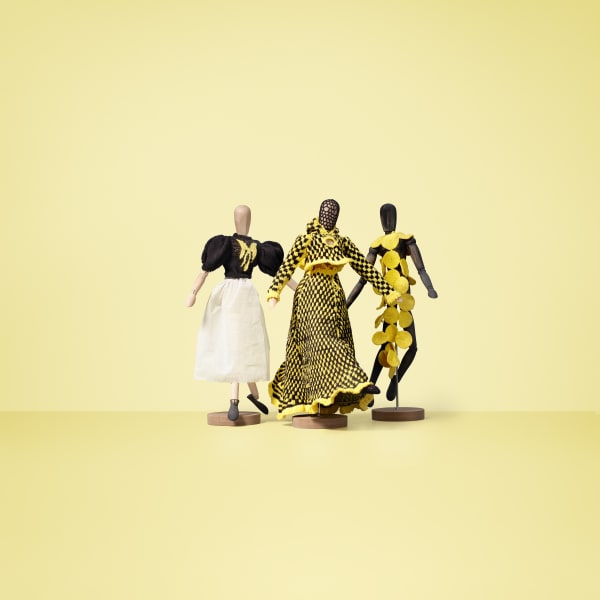 tre dockor med stickade kläder av Ann Bonander Looft, gul bakgrund.