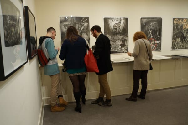 Photograph of gallery visitors looking through binders of Sue Coe's prints at the opening of the exhibition "Mad as Hell," 2012